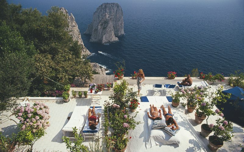 Sunbathers lounge on the white-painted terrace of Il Canille, built into the rocks of Pizzolungo overlooking the waters off the coast of the island of Capri, Italy, in August 1980. Il Canille is the villa owned by Italian tailor and fashion designer Umberto Tirelli (1928-1992). (Photo by Slim Aarons/Getty Images)